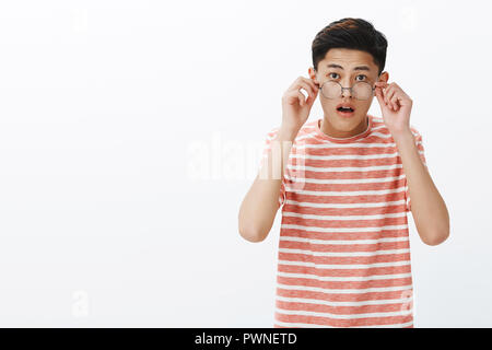 Portrait de surpris et émerveillé young cute asian male student taking off verres impressionnante audience nouvelles inattendues, bouche ouverte de surprise à l'écoute de dernière rumeurs enthousiastes sur fond blanc Banque D'Images