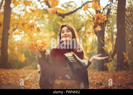 Happy girl lance de l'automne feuilles d'érable en automne forêt, smiling Banque D'Images