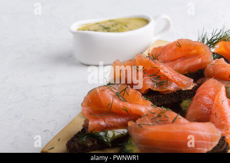 Gravlax de saumon fumé maison, sauce à la moutarde et l'aneth sur pain de seigle grillé, délicieux apéritif servi sur planche à découper en bois Banque D'Images