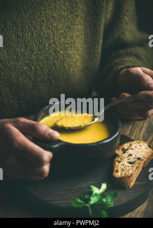 L'homme en vert foncé pull hiver manger le maïs sucré et les crevettes soupe chaudrée de bol noir avec du pain grillé, close-up. Automne ou hiver réchauffement de la nourriture Banque D'Images