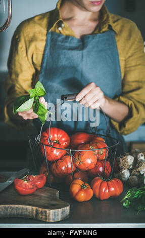 Tablier en lin femme holding basket with fresh heirloom tomatoes pour la cuisson de la sauce tomate, tomates en conserve ou de pâtes au basilic et l'ail en cuisine c Banque D'Images