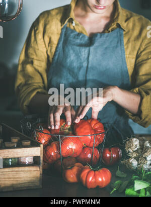 Tablier en lin femme sortant de tomates heirloom mûres panier pour la cuisson de la sauce tomate, tomates en conserve ou de pâtes au basilic et l'ail en cuisine Banque D'Images