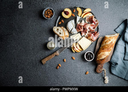 Plaque avec fromage et jambon, parmesan camamber, fromage de chèvre, jambon, de la baguette et des collations. Vue de dessus, fond sombre Banque D'Images