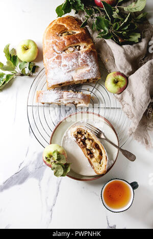 Des tranches de pâte feuilletée strudel aux pommes Tarte sur grille de refroidissement servi avec des pommes mûres, branches, le sucre en poudre, tasse de thé plus de texte en marbre blanc Banque D'Images