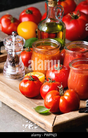 Variété de trois des sauces tomates en pots de verre avec des ingrédients ci-dessus. Différents types de tomates, basilic, huile d'olive, poivre, sel dans le bac en bois Banque D'Images