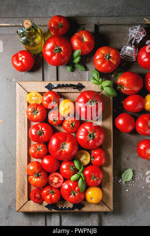 Variété de tomates fraîches mûres jardinage biologique différents types et couleurs spot avec de l'eau, les feuilles de basilic dans le bac bouteille d'huile d'olive, poivre et sel Banque D'Images