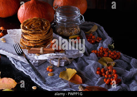 Concept d'automne. Crêpes à la citrouille avec garniture au caramel, avec des citrouilles, des feuilles sur un fond sombre. Close up Banque D'Images