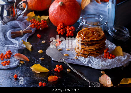 Concept d'automne. Crêpes à la citrouille avec garniture au caramel, avec des citrouilles, des feuilles sur un fond sombre. Close up Banque D'Images