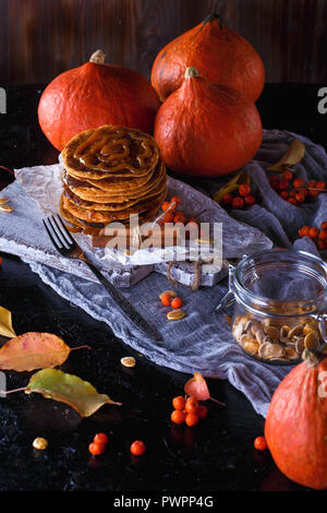 Concept d'automne. Crêpes à la citrouille avec garniture au caramel, avec des citrouilles, des feuilles sur un fond sombre. Close up Banque D'Images