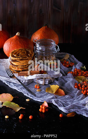 Concept d'automne. Crêpes à la citrouille avec garniture au caramel, avec des citrouilles, des feuilles sur un fond sombre. Close up Banque D'Images