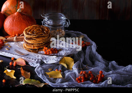 Concept d'automne. Crêpes à la citrouille avec garniture au caramel, avec des citrouilles, des feuilles sur un fond sombre. L'espace de faire face Banque D'Images