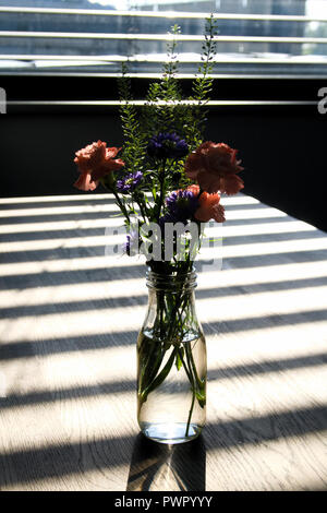 L'accent doucement de fleurs dans vase en verre plein d'eau sur la table vide en bois avec des ombres sur la table horizontale et superbe soleil venant d'un w Banque D'Images