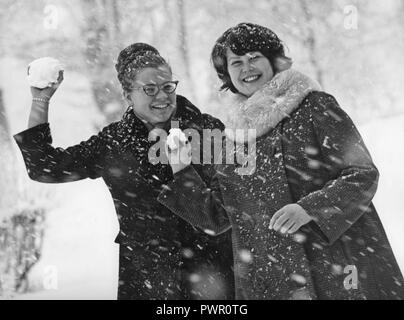 L'hiver dans les années 1960. Deux jeunes femmes vise à jeter et à propos de boules de neige sur le photographe. La neige tombe et ils sont habillés avec des manteaux d'hiver. Suède 1964 Banque D'Images