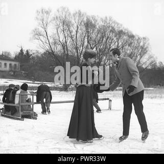 Figure skating au tournant du siècle, 1800-1900. Un couple est photographié ensemble lorsque vous l'extérieur. Dans l'arrière-plan un swing typique traîneau avec les enfants qui jouent avec elle. Photo probablement prise sur un plateau de tournage. Suède 1952. Kristoffersson Photo ref BF53-1 Banque D'Images