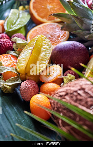 Fruits exotiques d'été - carambole, ananas, noix de coco, mangue, kiwi, les moitiés d'orange sur une feuille tropicale verte. Banque D'Images