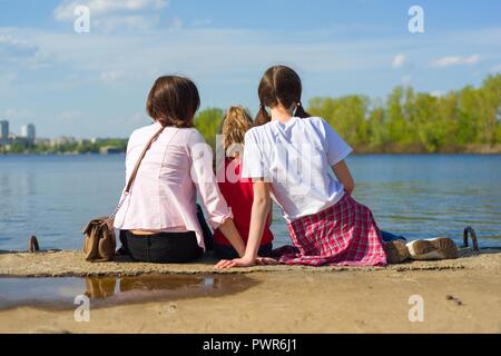 L'extérieur portrait de mère et deux filles. En regardant l'eau, vue de dos. Fond nature, parc, rivière. Banque D'Images