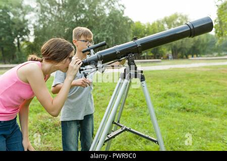 Adolescents Enfants avec Hubble regardez le ciel dans la nature. Banque D'Images
