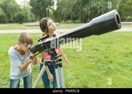 Adolescents enfants dans le parc à la recherche à travers un télescope. Banque D'Images