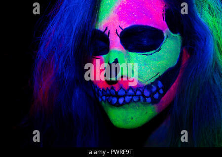 Femme avec son visage peint avec neon make-up avec un crâne design pour halloween Banque D'Images