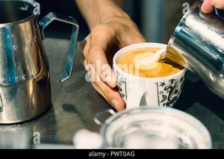 Close-up d'un barista pouring hot mâles mains mousse de lait sur une tasse de Latte art cappuccino. Banque D'Images