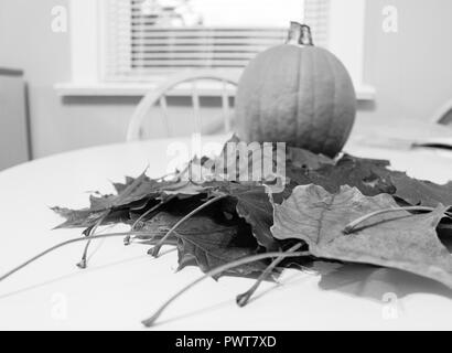 Photo en noir et blanc des feuilles d'automne et d'une citrouille tarte sur table de cuisine Banque D'Images