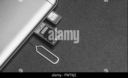 Téléphone mobile et d'emplacements ouverts pour nano cartes SIM, lecteur micro SD et clé de métal sur fond gris avec copie espace, photo en noir et blanc Banque D'Images