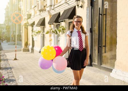 Adolescente de fille à l'école secondaire avec des ballons, à l'uniforme scolaire avec des lunettes va le long de la rue de la ville. Début des cours. Banque D'Images