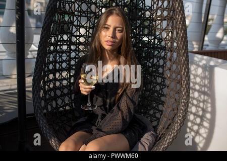 Jeune femme assise sur une chaise sur la terrasse d'un restaurant avec un verre de vin. Banque D'Images