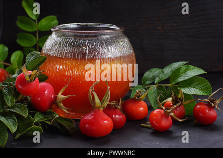 Confiture de cynorhodon lumineux dans un pot sur l'arrière-plan de feuilles et de Wild Rose de baies. Banque D'Images