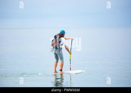 Homme de race blanche, vue arrière, isolé en mer, bénéficiant d'activités de plein air populaires, stand up paddle (SUP) surf sur des vacances d'été, Pays de Galles, Royaume-Uni. Banque D'Images