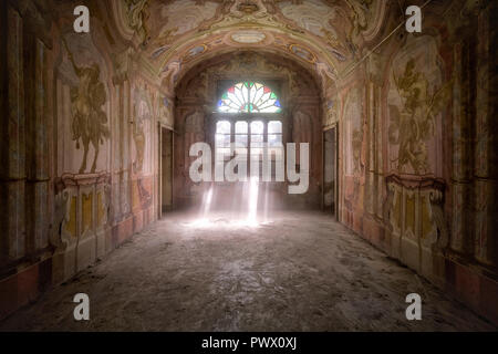 Vue intérieure d'une chambre dans une villa abandonnée en Italie avec des fresques et des faisceaux de lumière filtrant à travers la porte. Banque D'Images