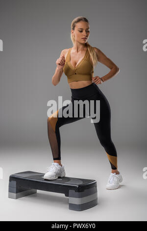 Jeune femme sportive exerçant sur l'étape de sélection sur gris Banque D'Images