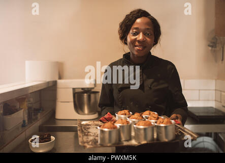 Smiling baker holding a tray de muffins dans sa cuisine Banque D'Images