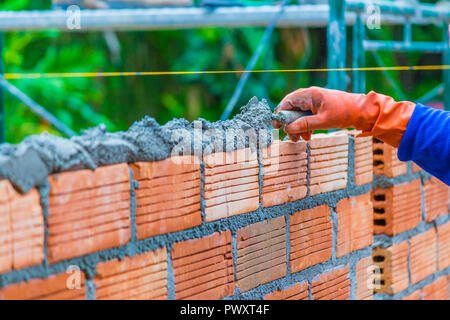 Main de travailleur de la construction d'une pâte de mortier sur le dessus de mur non fini la préparation de la prochaine couche de briques Banque D'Images