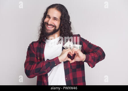 Faire la charité Kidness de jeunes adultes chemise à carreaux rouge et long cheveux bouclés debout, montrant sign coeur avec les doigts et sourire à pleines dents. Dans Banque D'Images