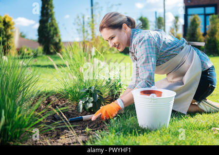 Transmission holding jardinier peu hoe dans ses mains alors que les mauvaises herbes jusqu'à l'arrachage Banque D'Images