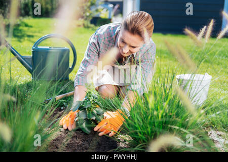 Smiling woman wearing apron beige assis près de son beau lit de jardin Banque D'Images