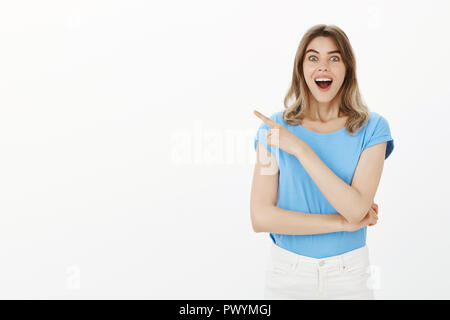 Fille n'a rien vu de mieux. Portrait of happy young woman impressionné avec cheveux blon, souriant et laissant tomber la mâchoire, faisant le coin en haut à gauche, d'être amusé et surpris de voir quelque chose fatntastic Banque D'Images