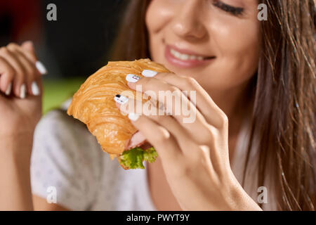 Libre de savoureux croissants avec les verts et le jambon en mains de jolie fille. Smiling woman gardant snack-, manger et profiter de la nourriture bonne dans un café au fond. Concept de délicieux repas rapides. Banque D'Images