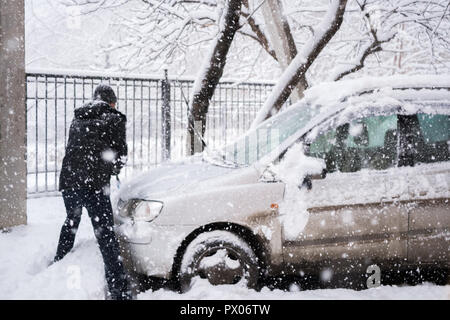 L'homme dans des vêtements sombres nettoie sa voiture lors de fortes chutes de neige. Banque D'Images