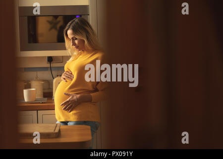 Pregnant woman touching her belly dans la cuisine Banque D'Images
