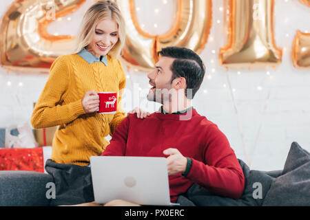 Happy man using laptop while woman holding tasse de café à la maison avec des ballons d'or 2019 pour le nouvel an Banque D'Images