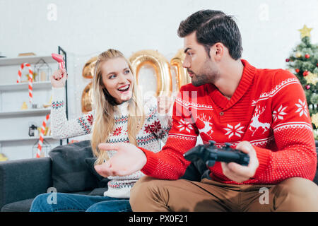 Jeune couple jouant avec les manettes de jeu vidéo la veille de Noël Banque D'Images