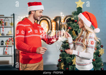 Couple heureux dans santa hats holding cierges et de trinquer avec les verres de champagne la veille de Noël Banque D'Images