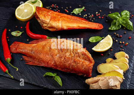 Rouge fumé à chaud de vivaneaux sur une plaque en pierre noire avec des épices, des herbes et des tranches de citrons, vue de dessus, close-up Banque D'Images