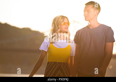 Jeune couple standing on river beach pendant le coucher du soleil Banque D'Images