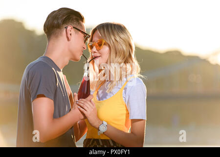 Couple drinking beverage avec deux pailles en plastique d'une bouteille sur la plage en soirée Banque D'Images