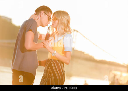 Couple drinking beverage avec deux pailles en plastique d'une bouteille sur la plage pendant le coucher du soleil Banque D'Images