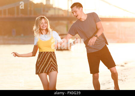 Laughing young couple having fun on river beach pendant le coucher du soleil Banque D'Images