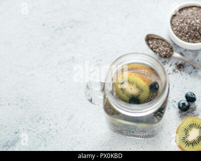 Vue du dessus de l'eau dans la région de chia pot Mason avec kiwi et blueberry sur fond de ciment gris. Chia infusé avec de l'eau detox de baies. L'espace de copie pour le texte. La saine alimentation, boissons, alimentation, concept detox Banque D'Images